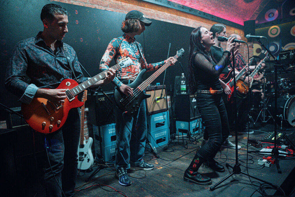 School of Rock Schulband live auf der Bühne – Gitarrist, Bassist und Sängerin spielen gemeinsam beim Konzert