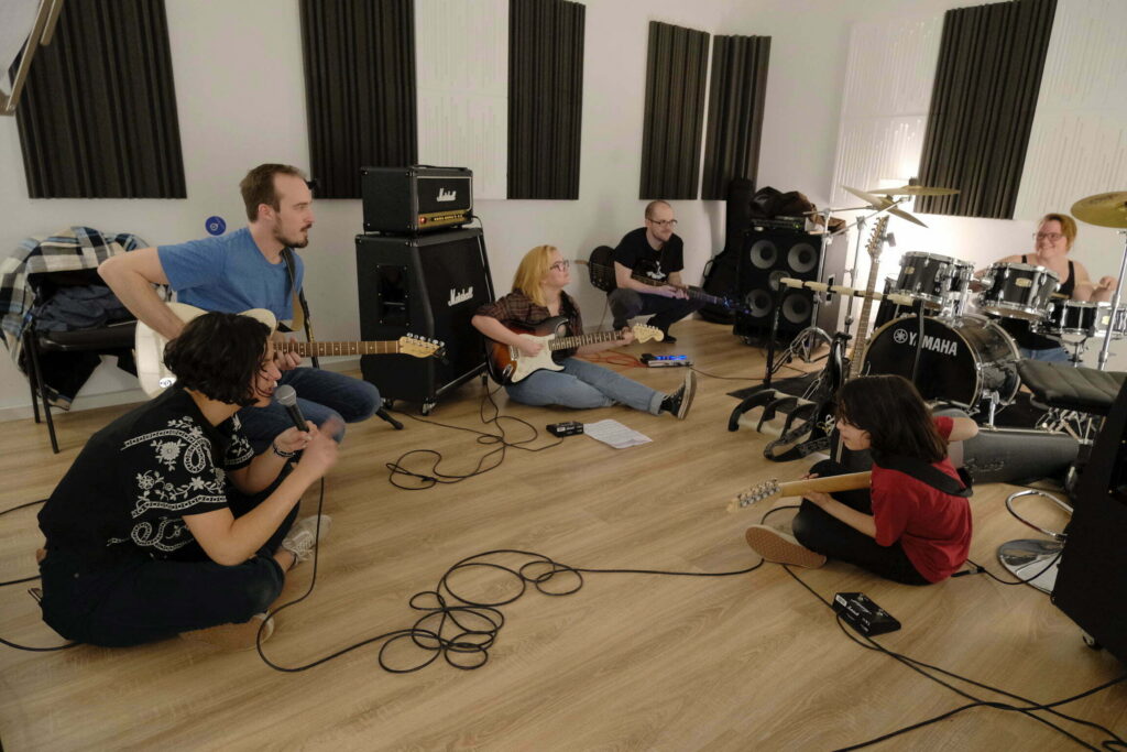 School of Rock Schulband bei der Probe – Schüler mit Gitarre, Bass, Mikrofon und Schlagzeug im Proberaum